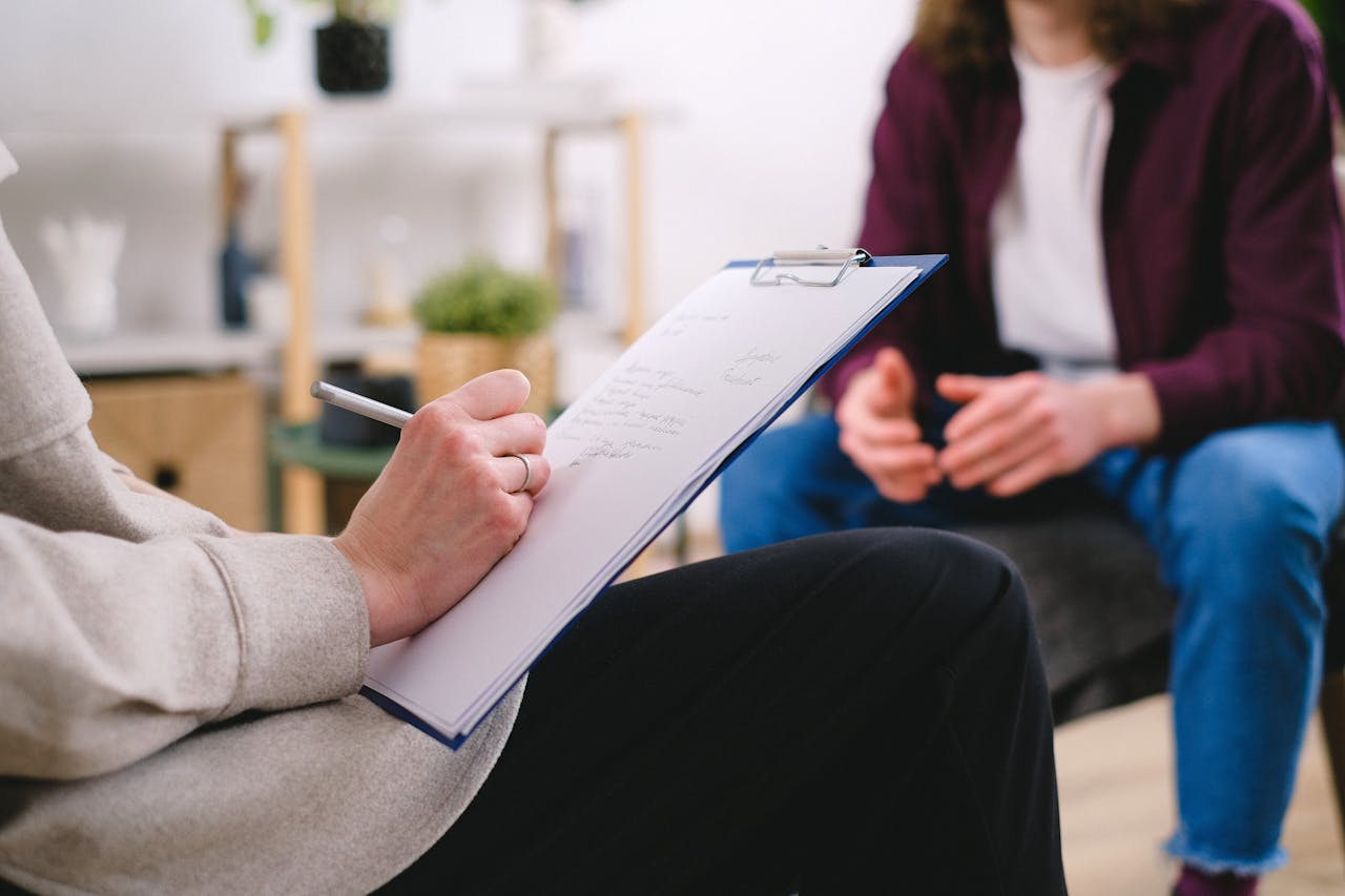 about-us-02 Close-up of a therapist writing notes on a clipboard while conversing with a patient.